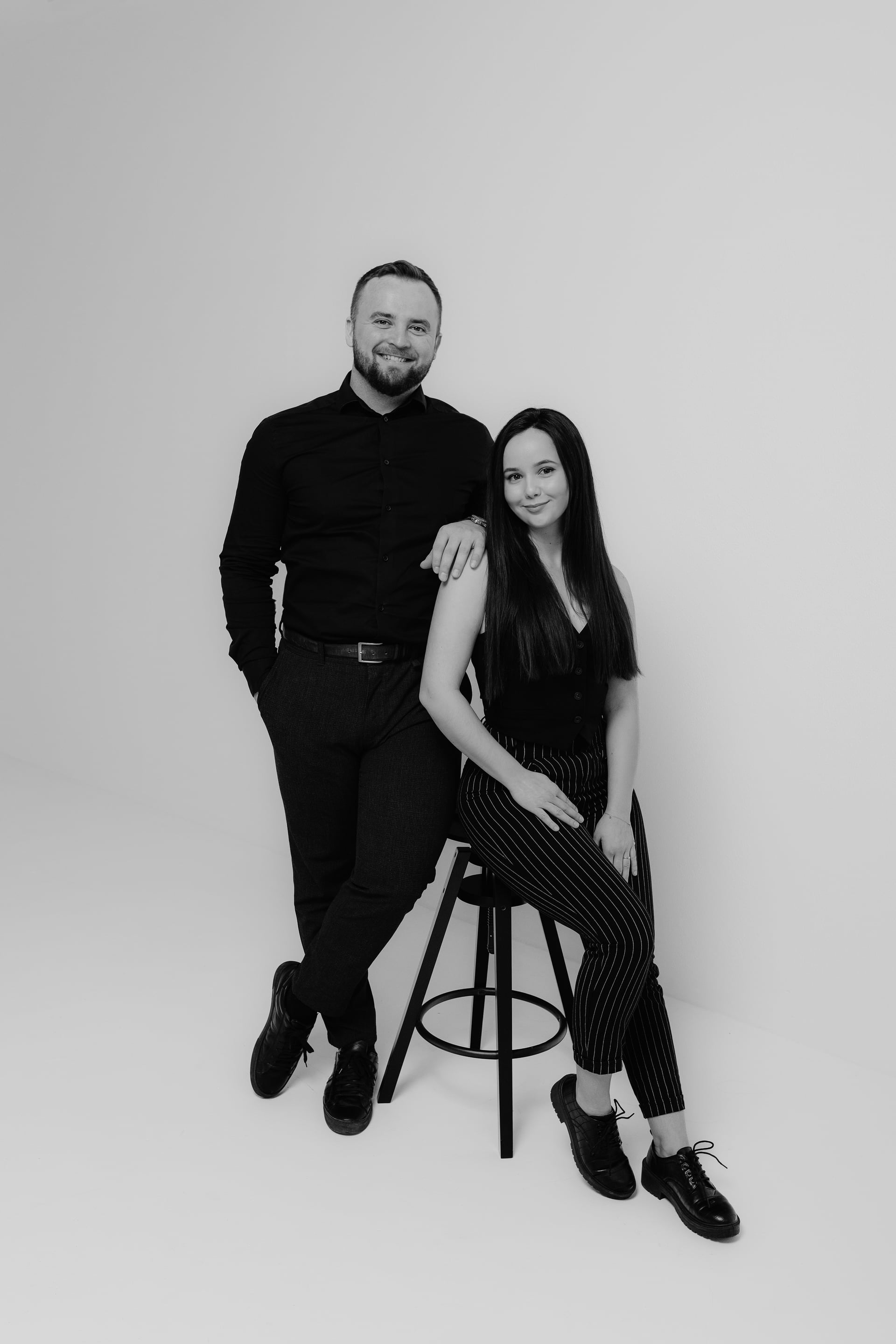 Michal a Andrea z fotografického dua Dve Duše — čiernobiely štúdiový portrét, on sa opiera o vysokú barovú stoličku, ona sedí na stoličke, obaja v čiernom